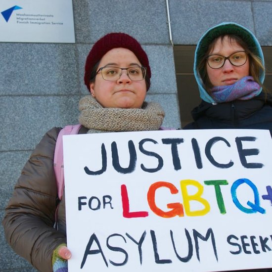 Image shows two Russian LGBT+ activists at protest, with protest sign that reads: "Justice for LGBTQ+ Asylum Seekers"